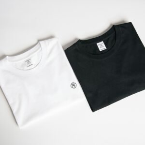 Two folded t-shirts, one black and one white, on a plain background in a minimalist style.